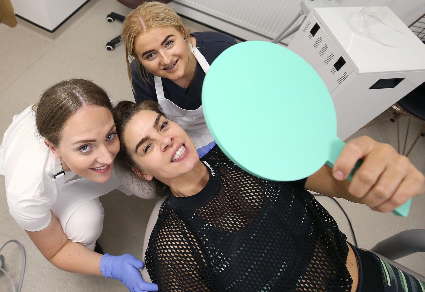 Two members of the team with a patient who is looking at her teeth in a mint-green hand mirror.